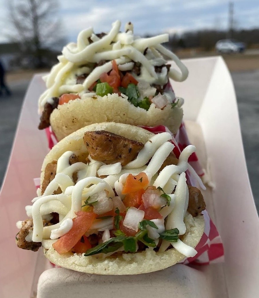 Two stuffed arepas topped with cheese, pico de gallo, and sauce