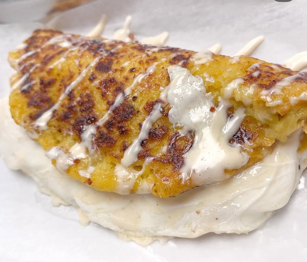 Cachapa folded around melted cheese with cream drizzled on top